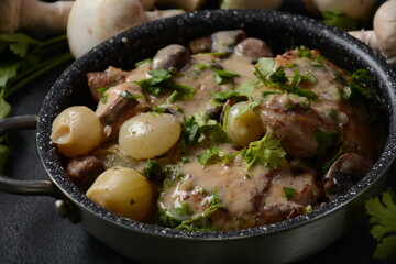 Fricassee - French Cuisine. Chicken stewed in a creamy sauce with mushrooms in casserole pan on a black table 
