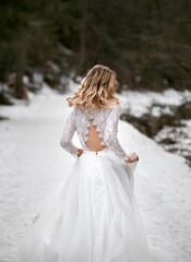 Fototapeta na wymiar blonde bride in snow park at winter wears minimalist white wedding dress