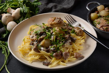 Fricassee - French Cuisine. Chicken stewed in a creamy sauce with mushrooms in a white plate on a black table 