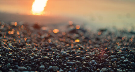 Close-up view of a pebble beach with blurred sea and sun background, selective focus