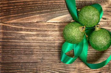 green Christmas balls and green silk ribbon on wooden background