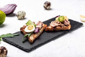 Close up Toasts with tuna. Italian bruschetta sandwiches with canned tuna, cucumber, quail eggs and onions on a light background, top view. Food recipe background