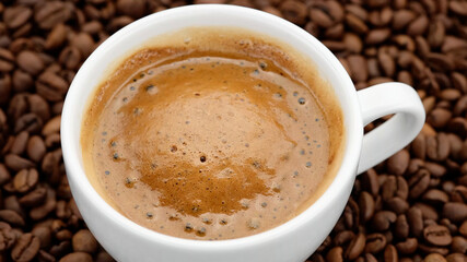 cup of black coffee with froth on coffee beans top view