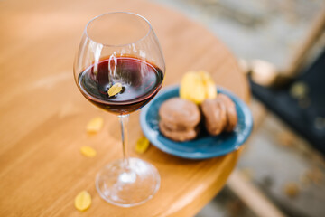 Glass of red wine and macaroons on the table outdoors the terrace with falling yellow foliage. Autumn mood concept