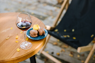 Glass of red wine and macaroons on the table outdoors the terrace with falling yellow foliage. Autumn mood concept