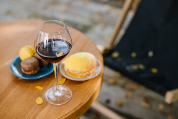 Glass of red wine and macaroons on the table outdoors the terrace with falling yellow foliage. Autumn mood concept