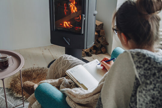 Young Woman  Write In Notebook Sitting In Armchair By Fireplace