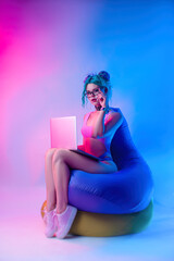 a woman in a bright bathing suit with blue hair is sitting on a chair bag with a laptop