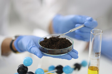 Glass cup with soil sample stands on hand in rubber glove in chemical laboratory closeup....