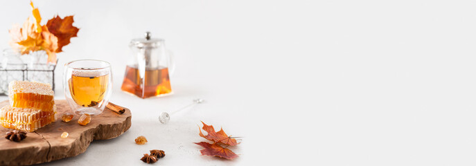 Autumn tea banner. Autumn hot tea with spices in glass cup, teapot, honey combs and falling leaves...
