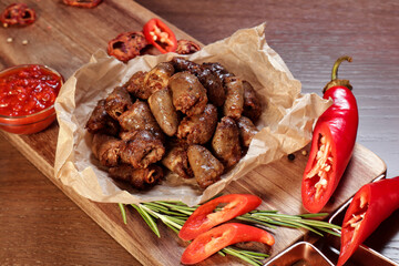 Fried chicken hearts with vegetables and spices on a wooden board.