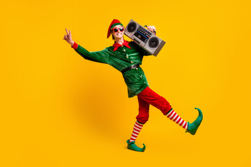 Full length body size view of his he nice attractive skinny cheerful cheery funny teenage guy elf carrying tape player dancing isolated over bright vivid shine vibrant yellow color background