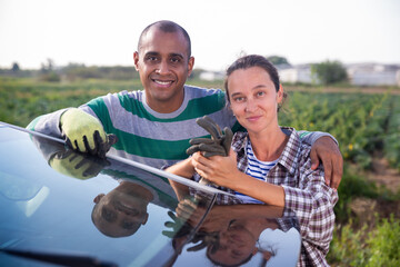 Portrait of successful smiling farmer couple standing outdoors near car on background with vegetable plantation on sunny fall day
