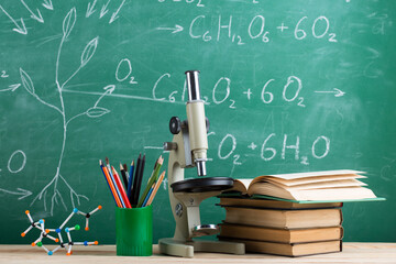 Education and sciences concept - books, molecule model and microscope on the desk in the auditorium, chalkboard background.
