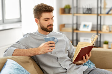 people and leisure concept - man reading book and drinking coffee at home