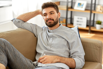 people and leisure concept - young man sitting on sofa at home