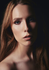 Fototapeta premium Dramatic portrait of beautiful young sad girl against black background. Close-up