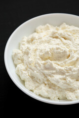 Tasty Ricotta Cheese in a white bowl on a black background, low angle view. Close-up.