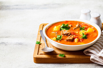 Soup with beef and vegetables in white plate on a wooden board, copy space. Traditional meat shurpa soup with vegetables and herbs.