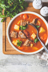 Soup with beef and vegetables in white plate on a wooden board. Traditional meat shurpa soup with vegetables and herbs, top view.