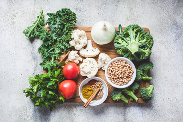 Cooking background of fresh vegetables, spices and beans. Raw ingredients for cooking vegetarian curry with vegetables and chickpeas on a wooden board, top view.