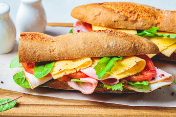 Baguette sandwiches with meat, cheese and vegetables on wooden board.