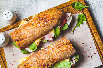 Baguette sandwiches with meat, cheese and vegetables on wooden board, top view.