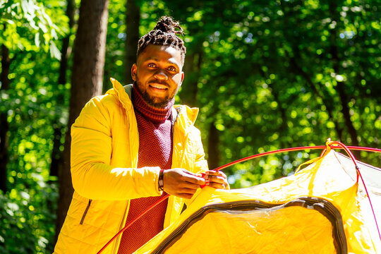 african american in yellow jacker putting on a tent in forest