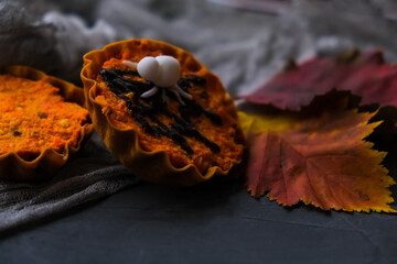 bright orange cupcakes in tartlets with a spider on background of gray web. next to autumn leaves. concept of Halloween