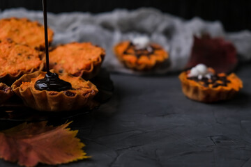 orange cupcakes in tartlets with spider on background of gray web. chocolate is poured on cake. concept of Halloween