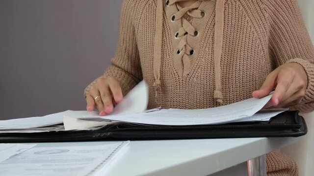Recorded information. A woman is engaged in office work. A woman works at an offside table. the woman searches for the necessary document, parses and checks the documents.
