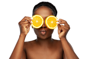 beauty, skin care and detox concept - beautiful african american woman making eye mask of oranges over white background