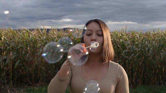 Pretty woman blowing soap bubbles in nature during sunlight and farm field in background.Slow motion.