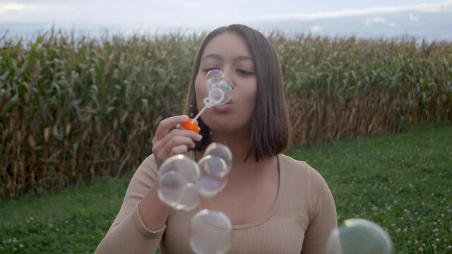 Young woman blowing bubbles on agriculture field during cloudy day in nature.Close up slow motion.