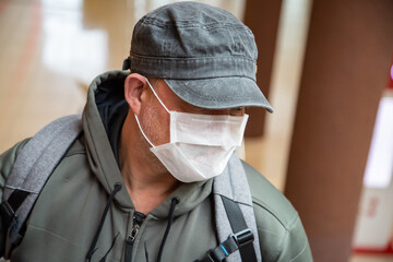 One middle-aged 40-45 European man wearing a properly worn white medical mask in a public place in a shopping center during the coronavirus epidemic, protecting against the Covid-19 pandemic