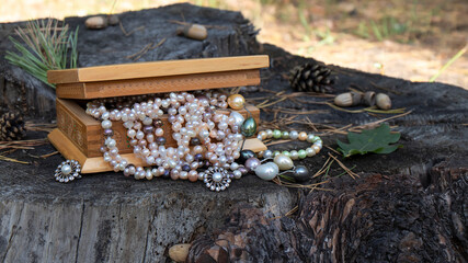 Colorful iridescent  pearl jewelry lies in an old carved wooden box on a dark cracked stump. ...