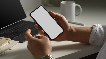 Male holding smartphone while sitting at workplace, include clipping path