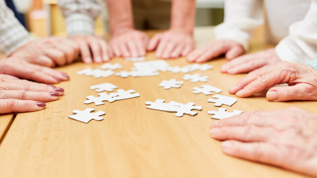 H&auml;nde von dementen Senioren beim Puzzle spielen auf dem Tisch im Altenheim