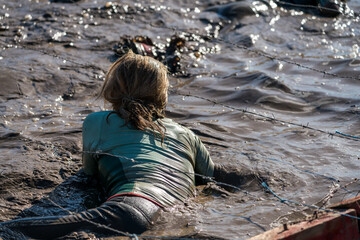 Female athlete crawling in mud under barbed wire at an obstacle course race