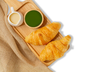 Croissants on wooden bread cutting board and sweetened condensed milk, green tea mug, with sackcloth over white background. Croissant french breakfast. Top view.