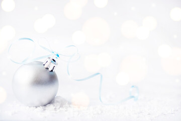 Christmas silver ball with ribbon on surface with snow and defocused lights with copy space