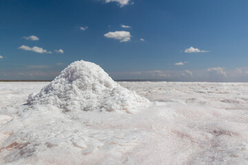 White salt bunch close-up shining on coast of salt lake with blurred blue sky background. Spa...