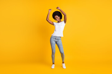 Full length body size photo of young female student with black skin listening music dancing with headphones wearing casual clothes smiling isolated on bright yellow color background