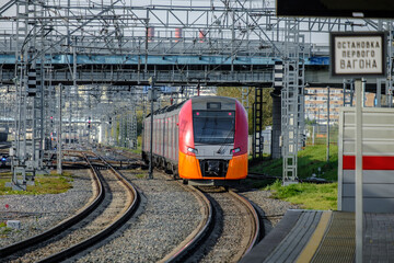 Naklejka premium A modern high-speed red train on a section of the Moscow Central Circle Line. Comfortable city rail public transport. Summer sunny day. The inscription in Russian means: Stop of the first car.