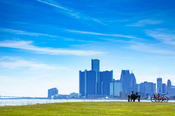 Fototapeta na wymiar Detroit river with view of downtown and lovely couple sit in the bench on Sunset Point over from Belle Isle