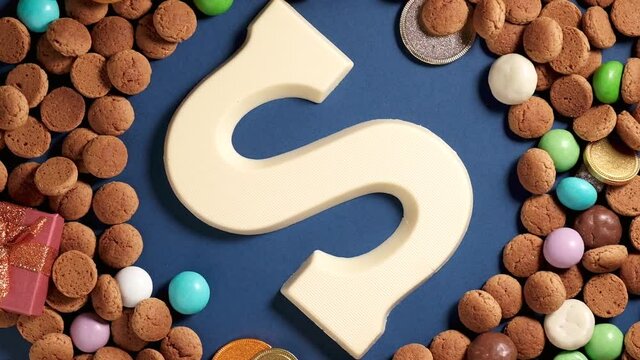 Rotation of kruidnoten, traditional sweets, strooigoed and white chocolate letter S. Background for Dutch holiday Sinterklaas. St. Nicholas day concept. FullHD video, top view