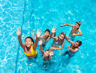 Children jump and play in swimming pool, splashing, lift hands smile view from above