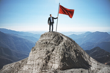 Obraz premium Businessman with red flag standing on mountain top.