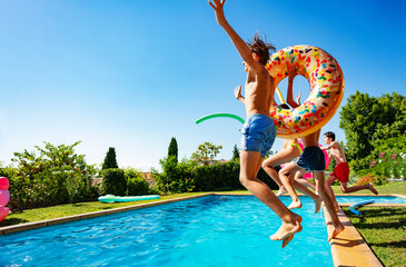 Happy many teenage kids with inflatable buoys dive into swimming pool jumping together view from...