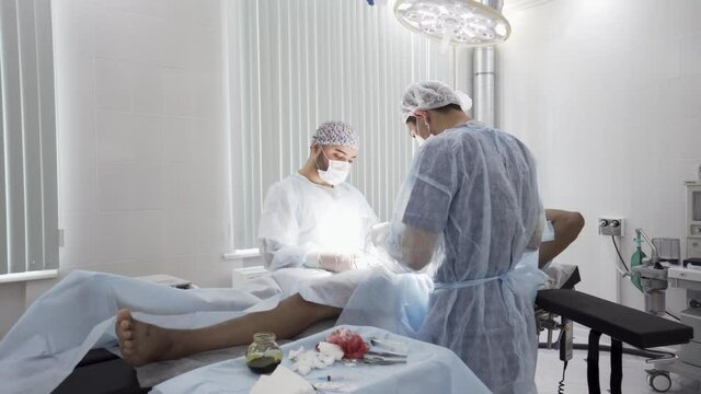 Gallbladder removal operation in the operation theatre. Action. Doctors helping patient during the surgery, bloody bandage is lying on the sterile table.